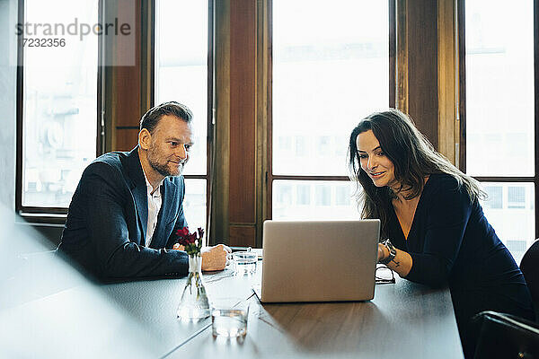 Lächelnde männliche und weibliche Kollegen diskutieren über Laptop im Sitzungssaal im Büro