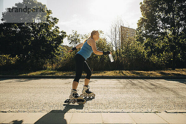 Weibliche Athletin Rollschuhlaufen auf der Straße während sonnigen Tag