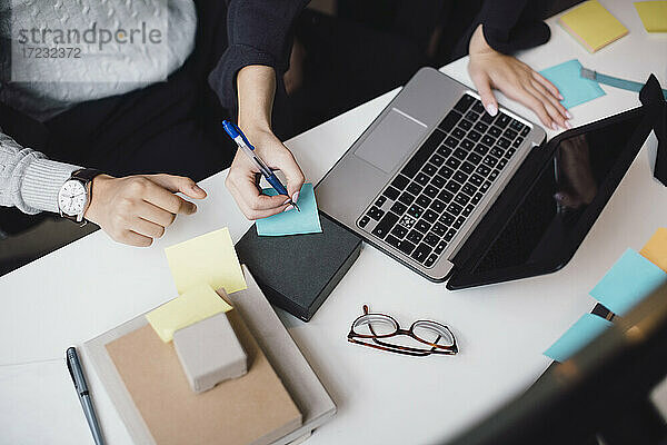 Cropped Hand der Geschäftsfrau Schreiben auf Haftnotiz von Laptop am Schreibtisch im Büro