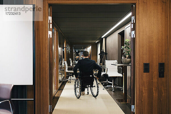 Rückansicht eines behinderten Geschäftsmannes auf einem Rollstuhl im Büro