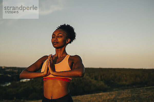 Junge Sportlerin meditiert gegen den Himmel bei Sonnenuntergang
