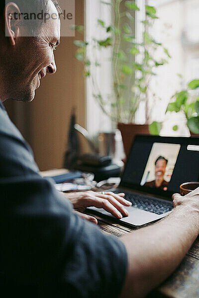 Lächelnder männlicher Unternehmer bei einem Videoanruf  der mit einem Kollegen zu Hause während COVID-19 diskutiert