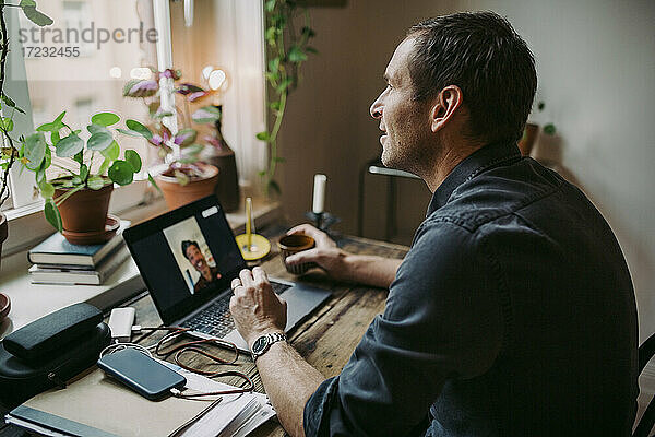 Geschäftsmann auf Video-Anruf mit männlichen Kollegen durch Laptop im Büro zu Hause