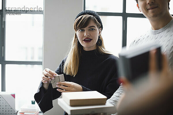 Weibliche Unternehmerin  die ein Produkt betrachtet  während sie neben einem männlichen Kollegen im Büro steht