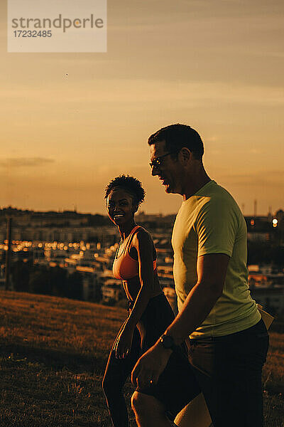 Lächelnde weibliche und männliche Athleten zu Fuß auf dem Land während des Sonnenuntergangs
