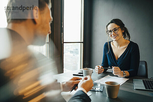 Lächelnde Geschäftsfrau  die mit einem männlichen Kollegen im Sitzungssaal im Büro diskutiert