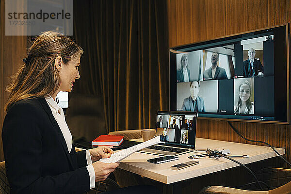 Geschäftsfrau diskutiert mit männlichen und weiblichen Kollegen auf Videoanruf durch Laptop im Büro