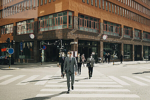 Geschäftsleute beim Überqueren der Straße an einem sonnigen Tag während COVID-19