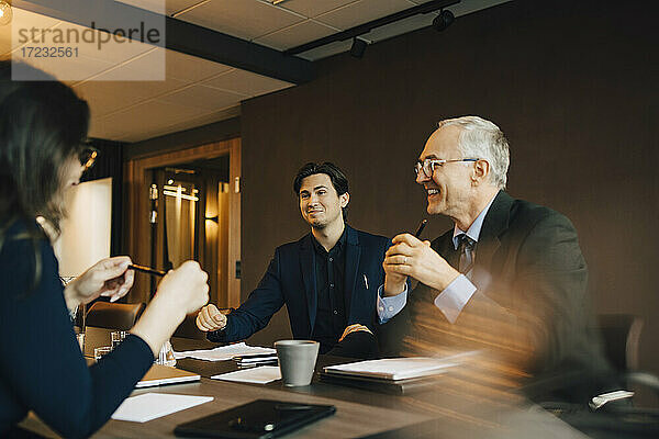 Lächelnder Geschäftsmann  der mit einem männlichen und einem weiblichen Kollegen im Sitzungssaal diskutiert