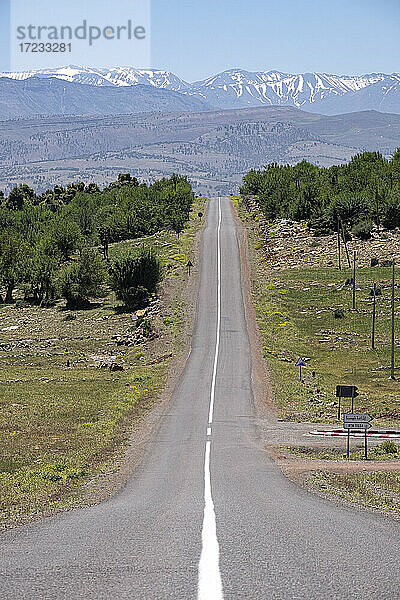 Lange geteerte Straße mit dem schneebedeckten Atlasgebirge im Hintergrund  Marokko  Nordafrika  Afrika