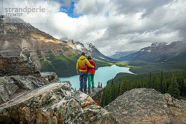 Paar umarmt sich  blickt in die Ferne  Ausblick auf türkisfarbenen Gletschersee umgeben von Wald  Peyto Lake  Rocky Mountains  Banff-Nationalpark  Provinz Alberta  Kanada  Nordamerika
