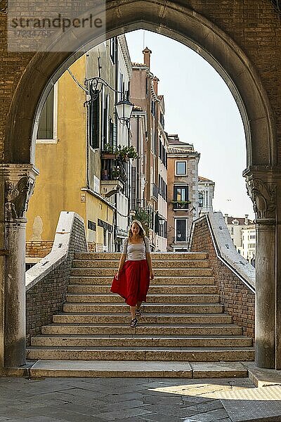 Junge Frau mit rotem Rock geht durch Torbogen  Mercato di Rialto  Venedig  Venetien  Italien  Europa