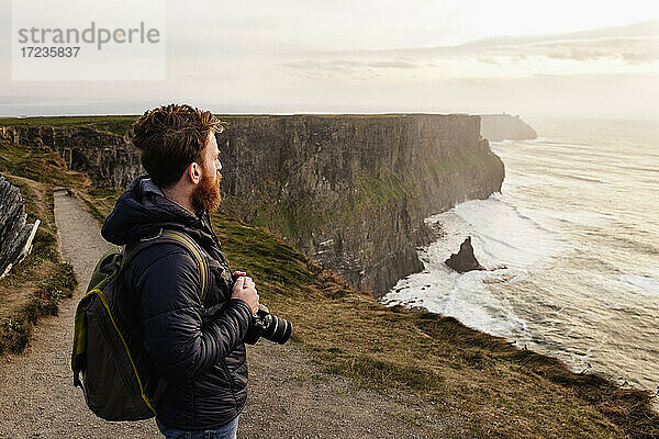Mittlerer Erwachsener Mann auf den Cliffs of Moher mit Kamera  The Burren  County Clare  Irland