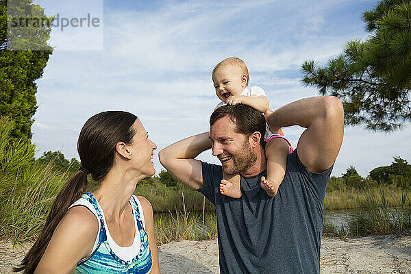 Mid erwachsenen Eltern mit Baby-Tochter auf mans Schultern von riverside