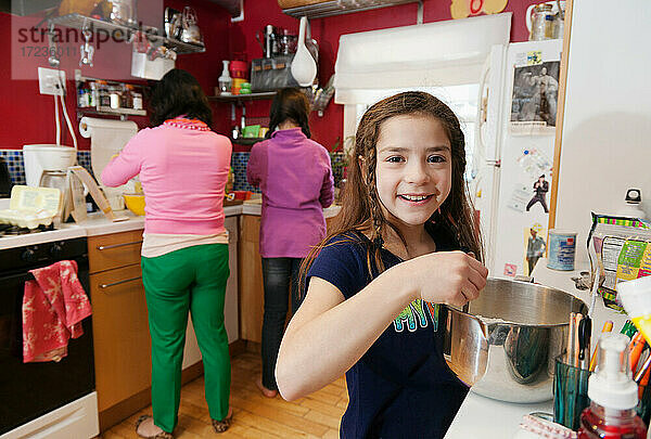 Mädchen in der Küche mit Mutter und Schwester im Hintergrund