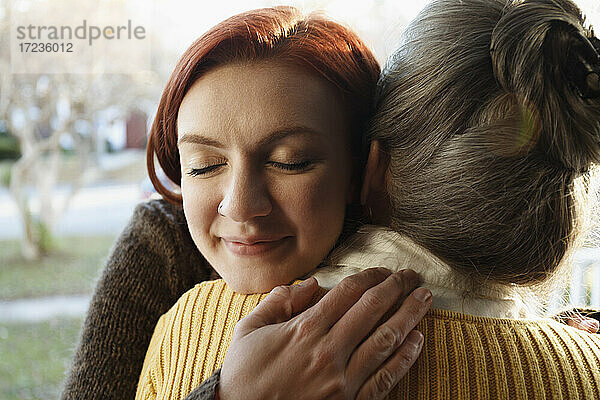Nahaufnahme einer älteren Frau und einer erwachsenen Tochter  die sich auf einer Veranda umarmen