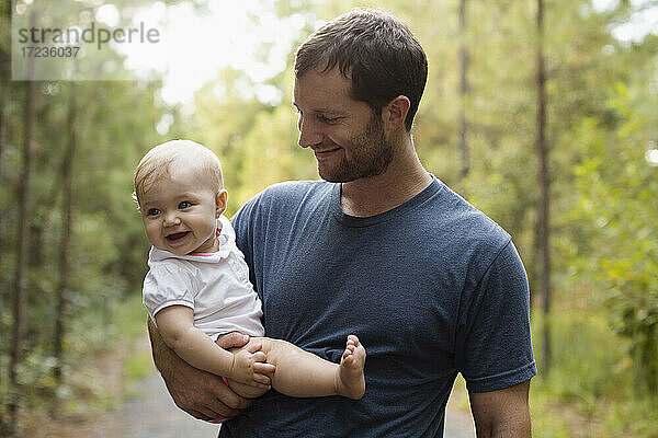 Glückliche Mitte erwachsenen Mann trägt Baby Tochter auf Waldweg