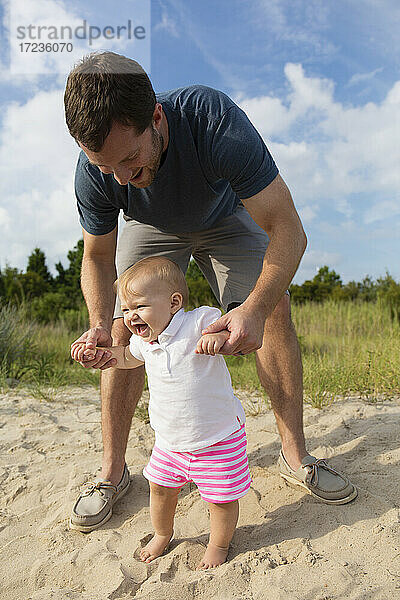 Mid erwachsenen Mann hält Baby Töchter Hände während watscheln in Sand
