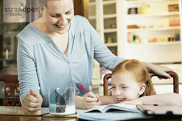 Mid erwachsene Mutter hilft Tochter mit Schule Hausaufgaben am Esstisch