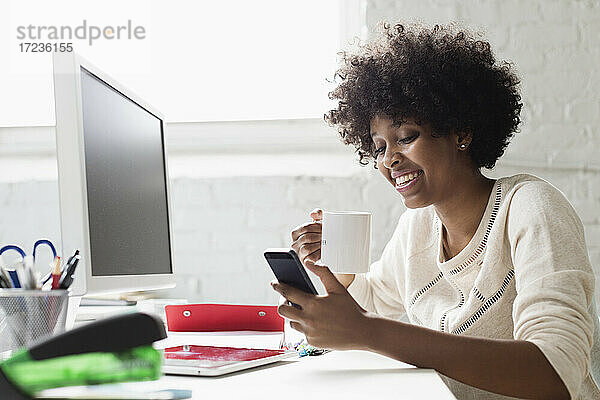 Junge Frau am Schreibtisch mit Kaffee mit Smartphone