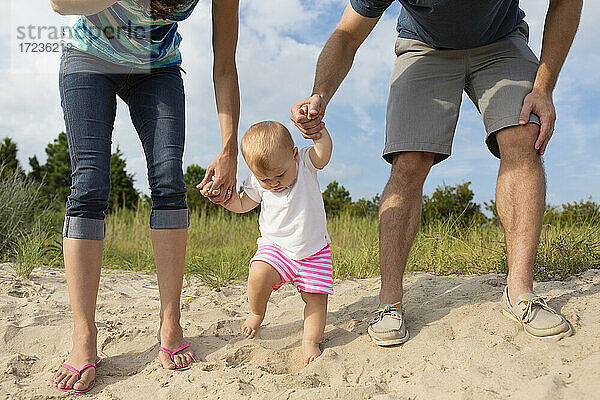 Mid erwachsenen Eltern halten Baby Töchter Hände während toddling in Sand