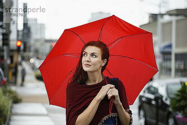 Junge Frau mit roten Haaren  hält roten Regenschirm