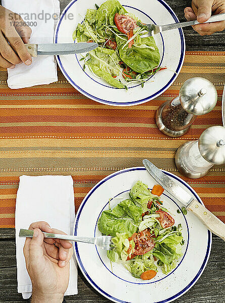 Overhead der Hände von Vater und Sohn essen Salat am Tisch