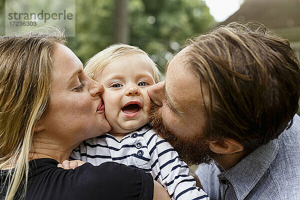 Mutter und Vater küssen Baby Mädchen auf die Wange  im Freien