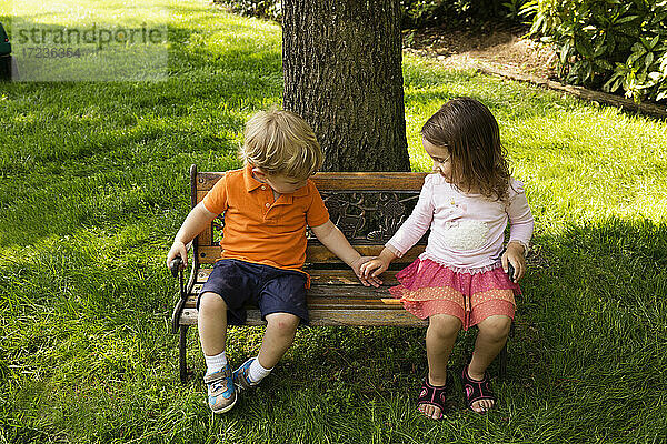 Männliche und weibliche Kleinkind Freunde halten Hände auf skalierten Parkbank