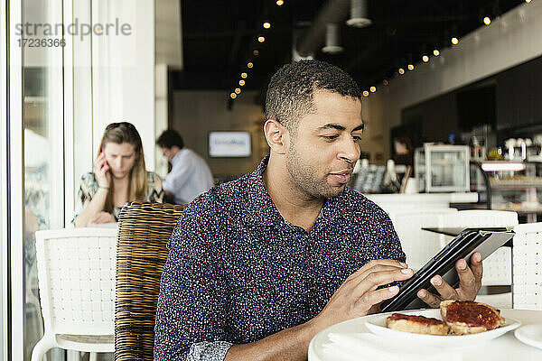 Junger Mann in einem Café  der ein digitales Tablet benutzt