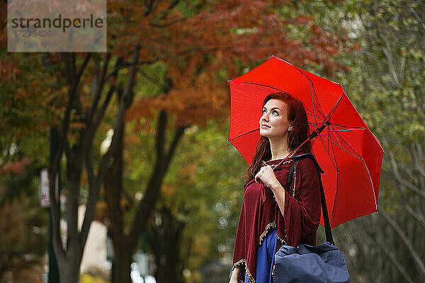 Junge Frau mit roten Haaren  hält roten Regenschirm