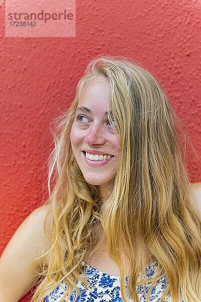 Portrait einer Jungen Frau mit langen blonden Haaren vor einer roten Wand  lacht  Insel Burano  Venedig  Venetien  Italien  Europa