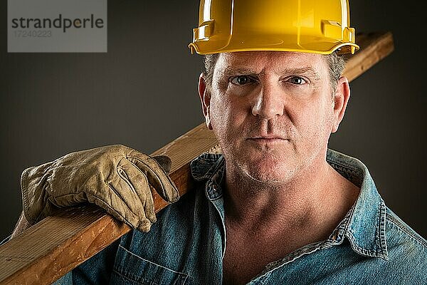 Portrait Bauarbeiter mit Schutzhelm  der eine Holzplanke hält