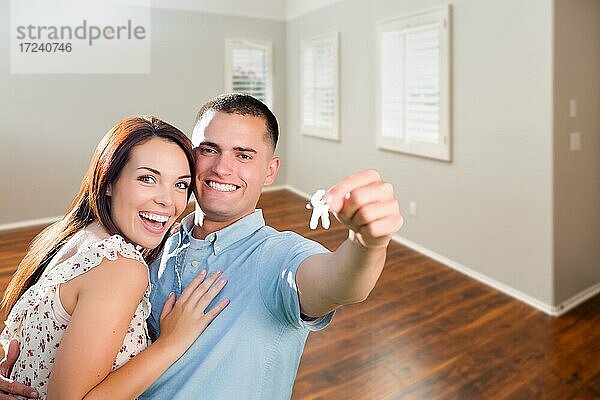 Junges Paar zeigt Hausschlüssel im leeren Zimmer des neuen Hauses