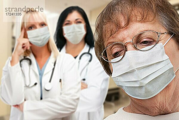 Ältere adultes Weibchen blickt nach unten  während Ärzte hinter ihr stehen und alle medizinische Gesichtsmasken tragen