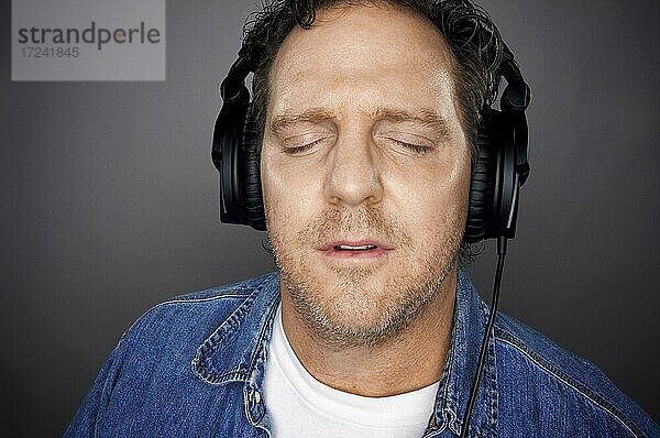 Mann mit geschlossenen Augen und Kopfhörern genießt seine Musik vor einem grauen Hintergrund