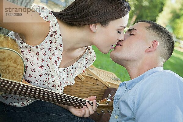 Zärtliches gemischtrassiges Paar mit Gitarre  das sich im Park küsst