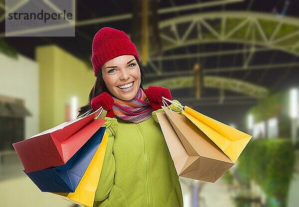 Hübsche warm gekleidete gemischtrassige Frau im Einkaufszentrum mit Einkaufstaschen