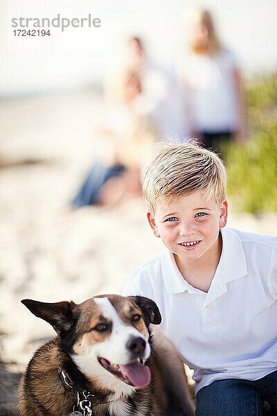 Hübscher Junge spielt mit seinem Hund am Strand