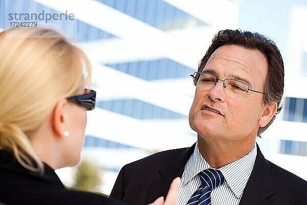 Aufmerksamer  gutaussehender Geschäftsmann in Anzug und Krawatte im Gespräch mit einer Kollegin im Freien