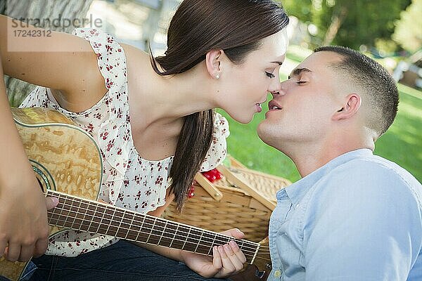 Zärtliches gemischtrassiges Paar mit Gitarre  das sich im Park küsst