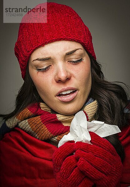 Kranke gemischtrassige Frau mit Wintermütze und Handschuhen  die sich die wunde Nase mit einem Taschentuch putzt