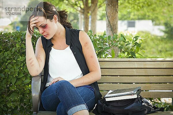 Traurige geschlagene und misshandelte junge Frau sitzt auf einer Bank in einem Park