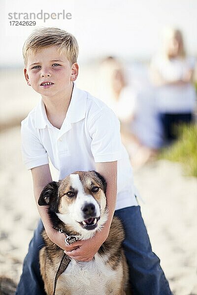 Hübscher Junge spielt mit seinem Hund am Strand