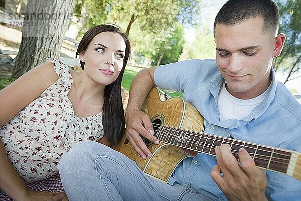 Glückliches gemischtrassiges Paar im Park  das Gitarre spielt und Lieder singt
