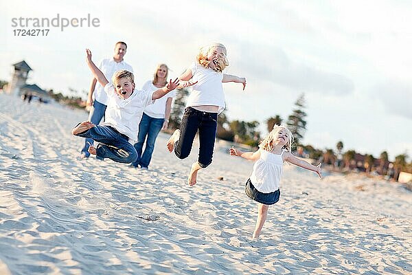 Glückliche Geschwisterkinder springen vor Freude am Strand  während die Eltern zusehen