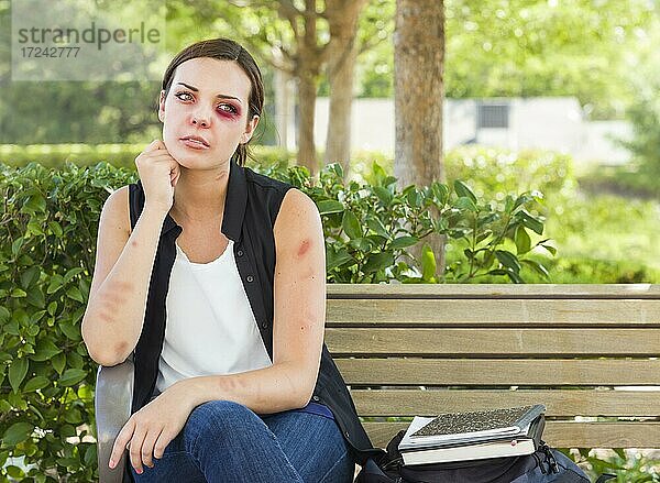 Traurige geschlagene und misshandelte junge Frau sitzt auf einer Bank in einem Park