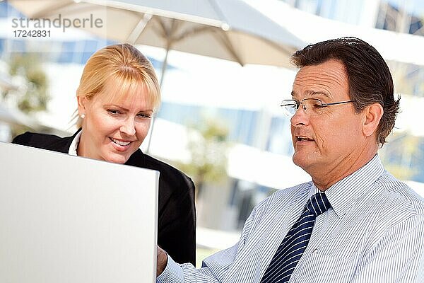Gutaussehender Geschäftsmann arbeitet auf dem Laptop mit attraktiven weiblichen Kollegen im Freien