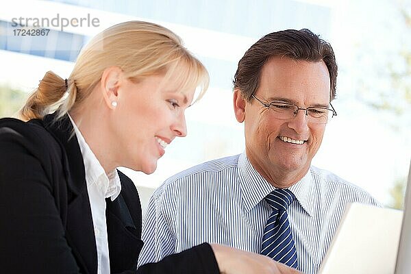 Gutaussehender Geschäftsmann lacht bei der Arbeit auf dem Laptop mit weiblichen Kollegen im Freien