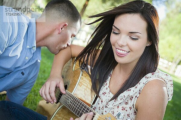 Glückliches gemischtrassiges Paar im Park  das Gitarre spielt und Lieder singt